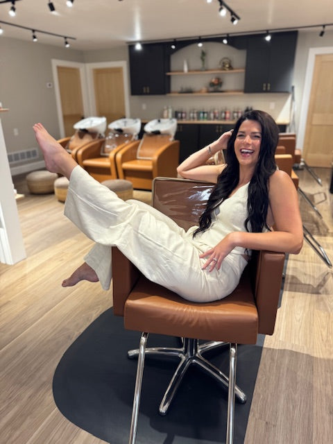 Woman in a white outfit sitting on a brown chair in a modern salon.